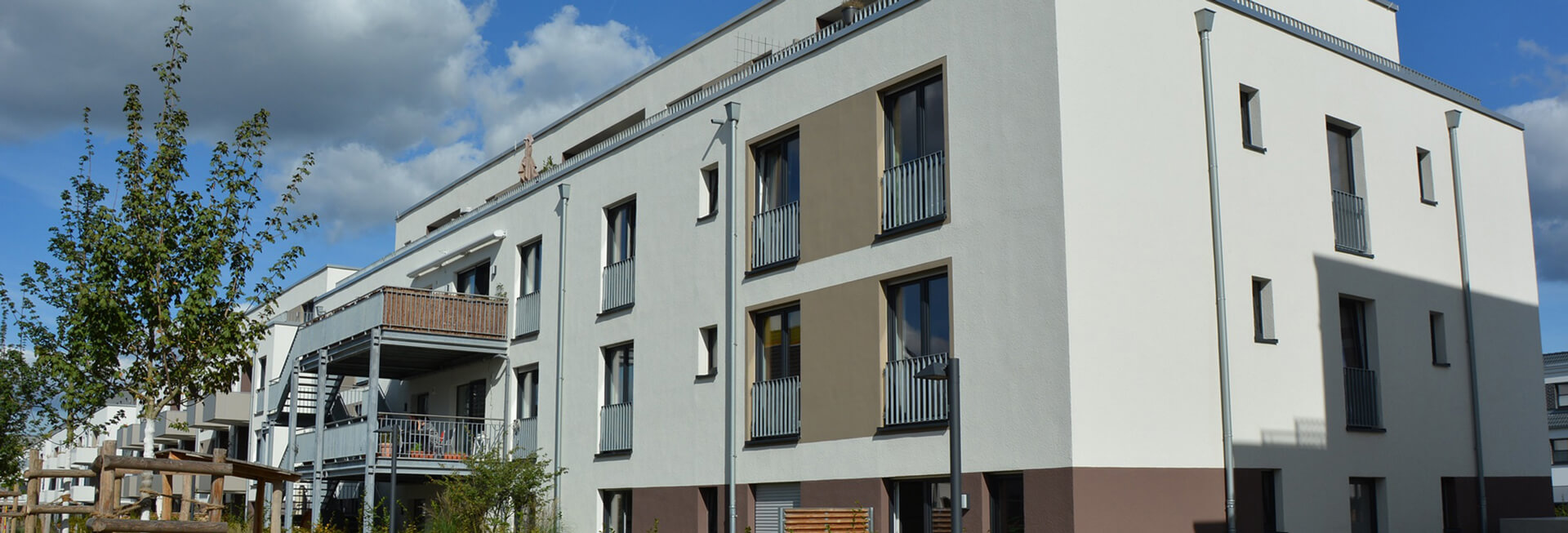 Blick von außen auf das inklusive Wohnhaus: Ein modernes, weiß gestrichenes Gebäude mit braunen Farbakzenten.