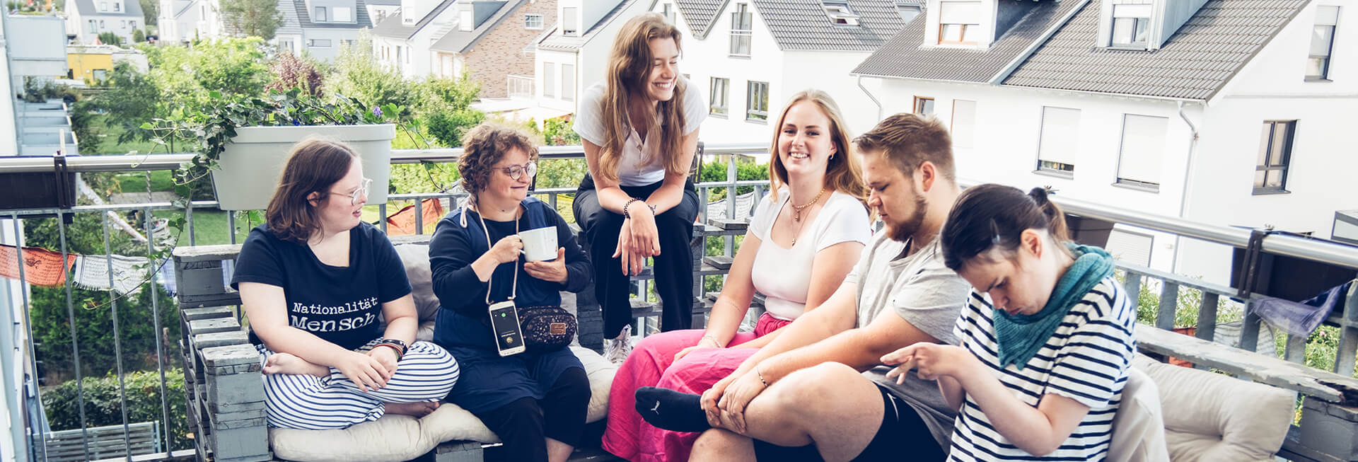 Sechs junge Bewohner einer inklusiven WG sitzen auf der Terrasse. Alle lächeln freundlich.