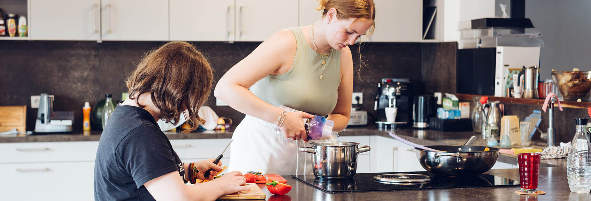 Zwei Mädchen, mit und ohne Behinderung, kochen gemeinsam in der Küche der inklusiven WG. Während die eine Gemüse schneidet, schüttet die andere Reis in einen Topf.