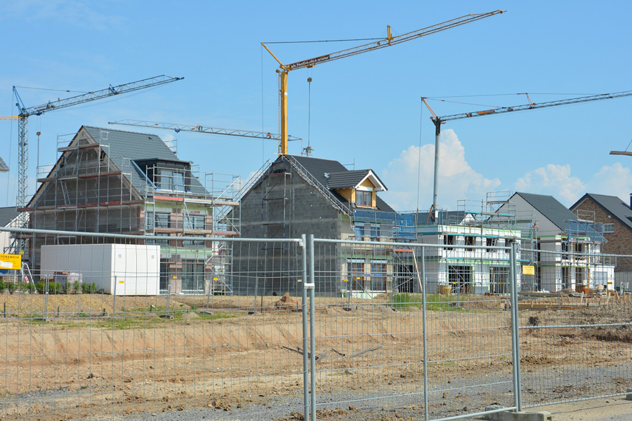 Blick auf eine Baustelle mit mehreren fast fertigen Häusern. Dazwischen stehen Kräne.